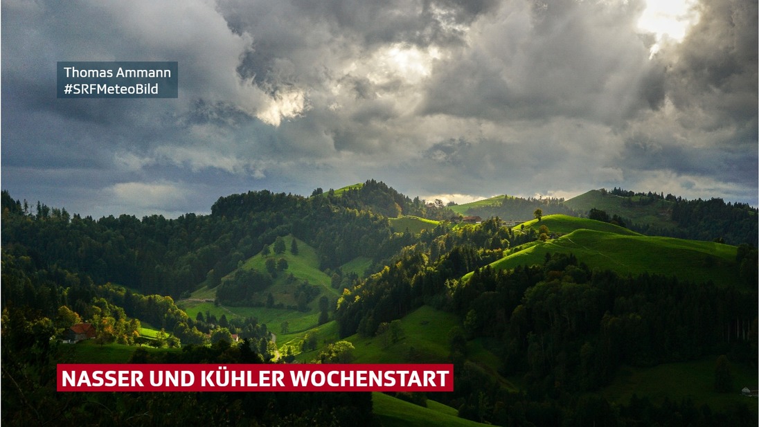 Blick auf eine hügelige Voralpenlandschaft unter dunklen Wolken.
