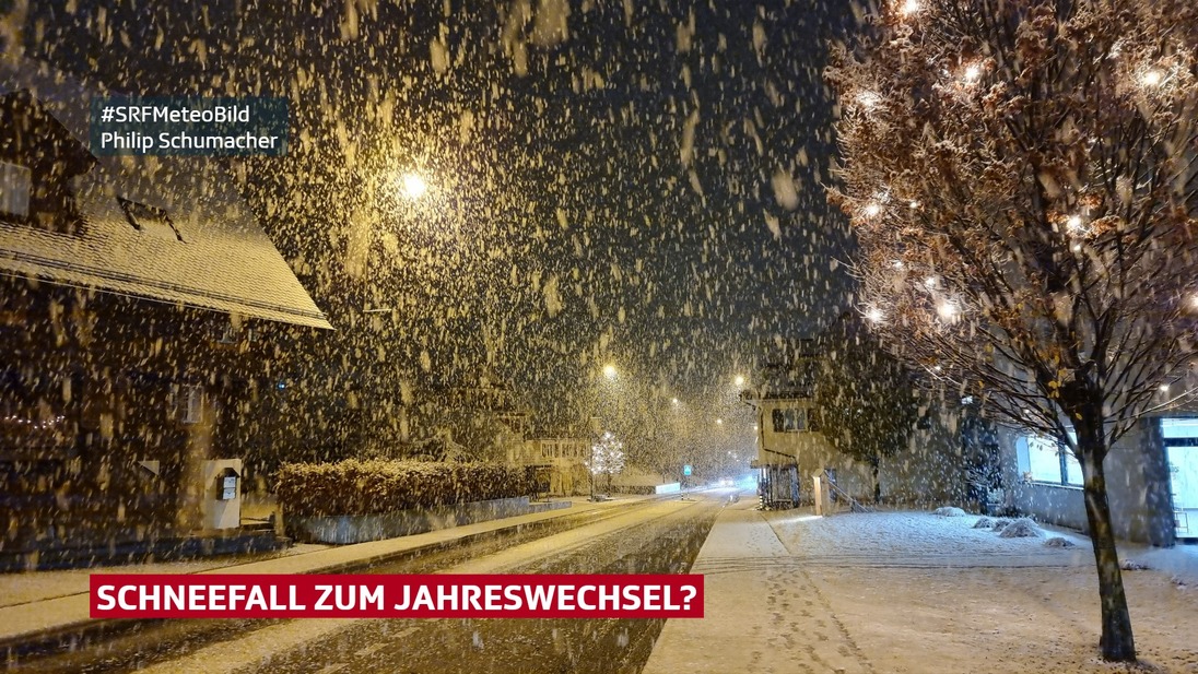 Nächtlicher Schneefall mit etwas Schnee auf Strasse und Trottoir.