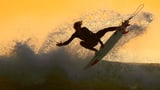 Ein Surfer in der Luft über einer Welle in der Abendsonne.