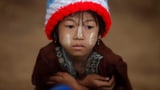Portrait eines Kindes mit bunter Mütze. Es blickt traurig.