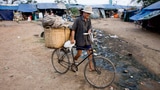 Ein Mann schiebt ein Velo in einem armen Quartier in Kambodscha.