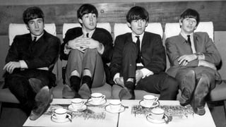Vier Männer sitzen auf einem Sofa und haben Teetassen vor sich.