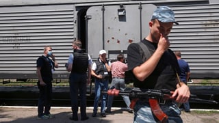 OSZE-Beobachter und Separatisten vor einem Kühlwaggon - sich die Nase zuhaltend.