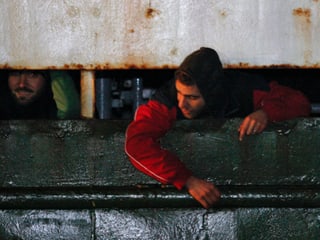 Zwei Flüchtlinge schauen aus einer Schiffsluker heraus.