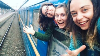 Drei junge Frauen schauen aus einem Zugfenster. 