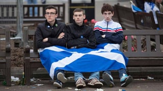 Drei junge Schotten sitzen enttäuscht mit der Flagge da.