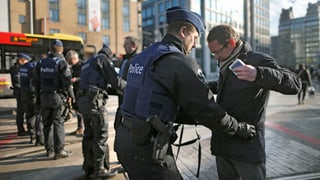 Mehrere Polizisten durchsuchen in Brüssel Passanten. 