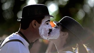 Zu sehen sind zwei als Mimen verkleidete Personen, ein Mann und eine Frau, die sich küssen.