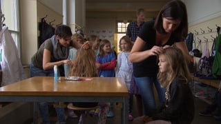 Drei Erwachsene prüfen die Köpfe einer Schulklasse. Drei Erwachsene prüfen die Köpfe einer Schulklasse.