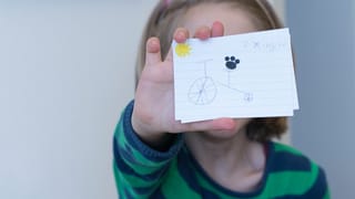 Ein Mädchen hält eine Karteikarte vors Gesicht. Darauf sind ein gezeichnetes Fahrrad und das Wort "zixingche" zu sehen. Ein Mädchen hält eine Karteikarte vors Gesicht. Darauf sind ein gezeichnetes Fahrrad und das Wort "zixingche" zu sehen.