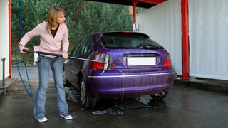 Eine junge Frau wäscht ihr Auto in einer Selbstbedienungsbox