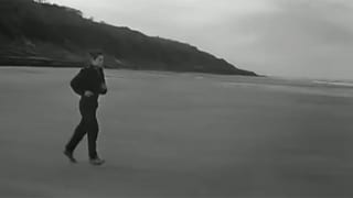 Schwarz-Weiss-GIF: Ein Junge im schwarzen Mantel rennt den Strand entlang.