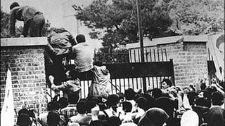 Leute klettern über die Botschaftsmauer in Teheran. Schwarzweiss-Foto.