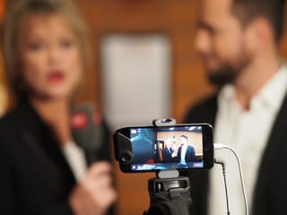 Smartphone mit Daniela Lager und Trauffer im Hintergrund.