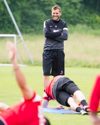 Sven Christ lachend und stehend, im Vordergrund Spieler bei Bodenübungen. Sven Christ lachend und stehend, im Vordergrund Spieler bei Bodenübungen.