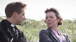 Szene aus Broadchurch: Zwei Männer und eine Frau sitzen mit Stühlen auf einer Wiese. Szene aus Broadchurch: Zwei Männer und eine Frau sitzen mit Stühlen auf einer Wiese.