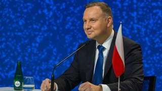  Andrzej Duda sitzend neben einer kleinen polnischen Flagge und Mikrofonen.