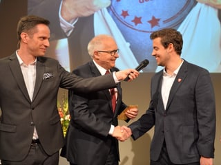 Adrian Küpfer hält Kevin Hirt das Mikrofon hin und Ruedi Matter gratuliert dem Preisträger.