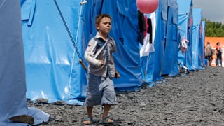 Ein Junge mit spielt mit einem rosaroten Ball zwischen blauen Zelten in einem Auffanglager.