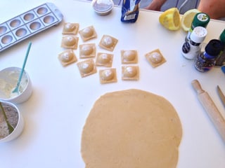 Tisch mit Ravioli und diversen Gewürzen. 