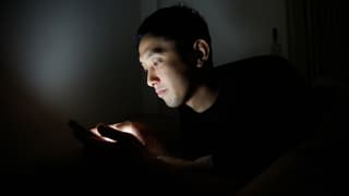 Ein asiatischer Mann in einem dunklen Raum starrt auf sein Handy. Ein asiatischer Mann in einem dunklen Raum starrt auf sein Handy.