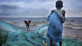 Ein Junge steht mit dem Rücken zum Betrachter auf einem Fischernetz und schaut aufs Meer.