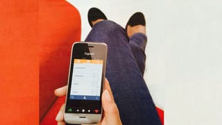 Eine Frau sitzt auf einem Sofa und hält ein schnurloses, smartphone-ähnliches Telefon in der Hand.