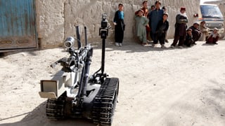 Ein Roboter sucht 2011 in Afghanistan nach Bomben, im Hintergrund betrachtet eine Gruppe Kinder ihn.
