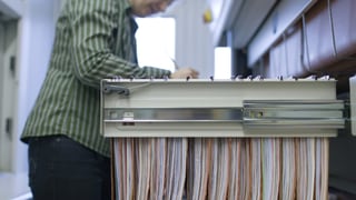 Eine Frau vor einer geöffneten Aktenschrank-Schublade mit Hängeregistern.