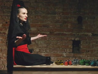 Eine rumänische Schauspierin sitzt auf einem Tisch, hat verschiedene Paare Schuhe vor sich und hält die Hände offen.