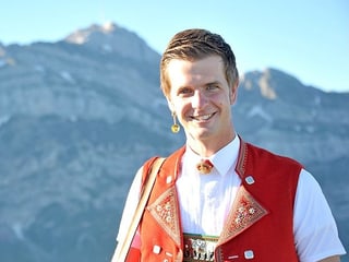 Nicolas Senn, rotes Appenzeller-Sennenchutteli, im Hintergrund Bergpanorama.