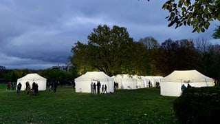 Leuchtende weisse Zelte mit Personen davor, die auf ihren Coronatest warten, sind in der Dämmerung zu sehen.