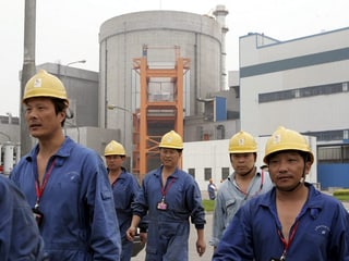 Fünf chinesische Atomarbeiter mit blauen Overalls und gelben Helmen vor einem Atomkraftwerk