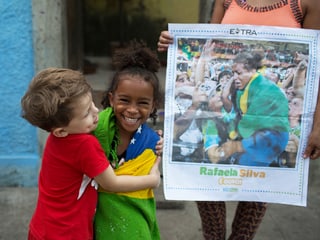 Rafaelas vierjährige Cousine Giovana Silva wird von einem Nachbarsjungen umarmt, daneben hält eine Frau einen Zeitungsartikel mit dem Bild der Siegerin.