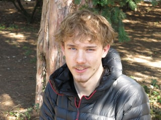 Junger Mann mit blonden Haaren und blauen Augen steht im Wald.