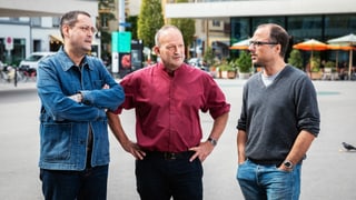 Drei Männer stehen auf einem Platz nebeneinander und sprechen miteinander. Drei Männer stehen auf einem Platz nebeneinander und sprechen miteinander.