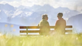 Zwei ältere Frauen sitzen auf einer Bank vor einem Bergpanorama