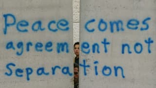 Zwei Jungen schauen hinter einer Mauer hervor auf der steht: "Peace comes agreement not Separation" Zwei Jungen schauen hinter einer Mauer hervor auf der steht: "Peace comes agreement not Separation"