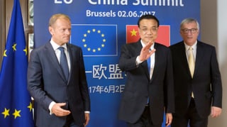 Drei Männer vor einer blauen Wand mit EU- und Chinaflagge.