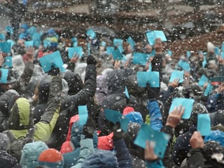 Erhobene Hände mit blauen Stimmzetteln im Schneeregen