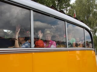 Ein paar Wanderinnen winken hinter den Fenstern des Oldtimer-Postautos.