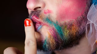 Ein Mann mit geschminktem Bart und roten Fingernägeln.