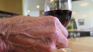 Hand einer älteren Person mit einem Glas Wein