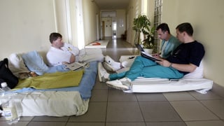 Männer auf Matrazen in einem Spitalgang.