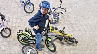 Ein Kind sitzt auf einem Kindervelo, darum herum liegen und stehen andere Kinderfahhräder.