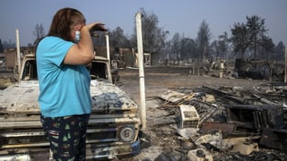Frau steht vor den Überresten verbrannter Autos und Häuser.