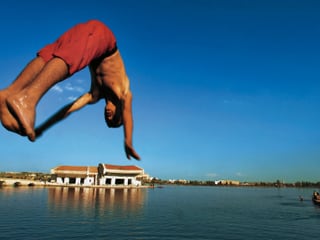 Ein Junge in roten Badehosen springt in einen See.
