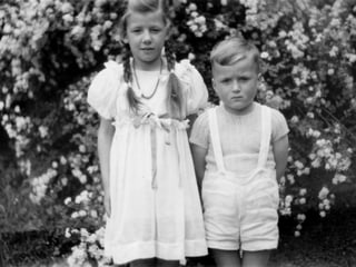 Zwei fein gekleidete Kinder posieren vor der Kamera.