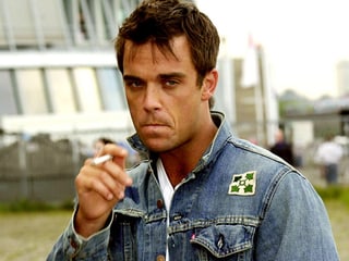 Robbie Williams in Jeansjacke, rauch eine Zigarette.