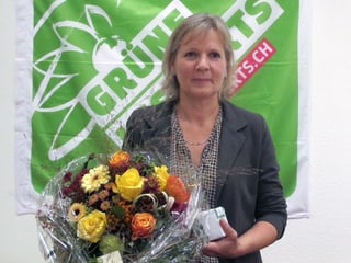 Frau mit Blumen vor einer grünen Fahne.